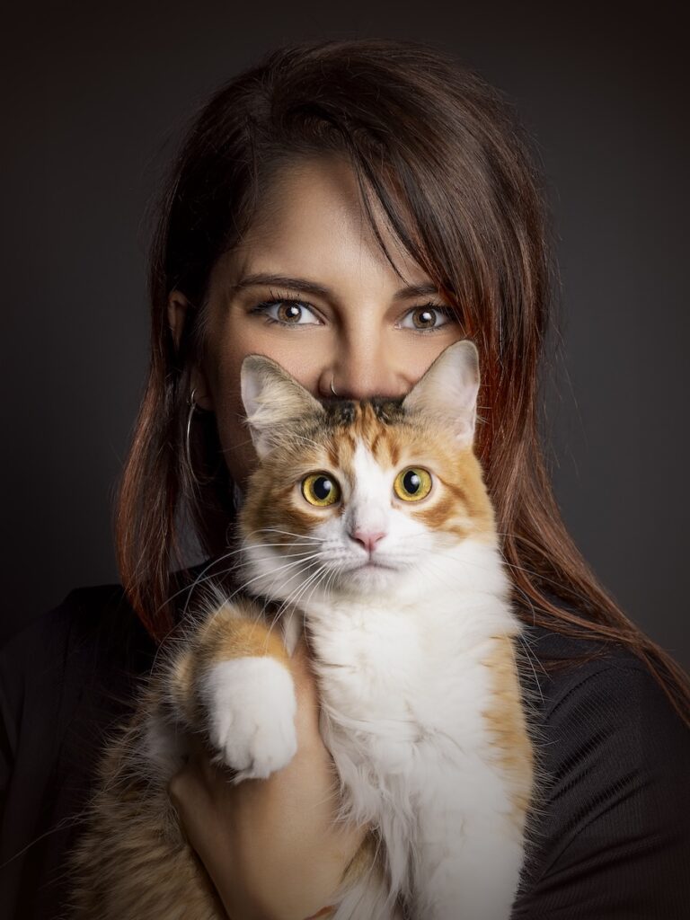 Fotografía de una mujer con su gata sobre un fondo en negro
